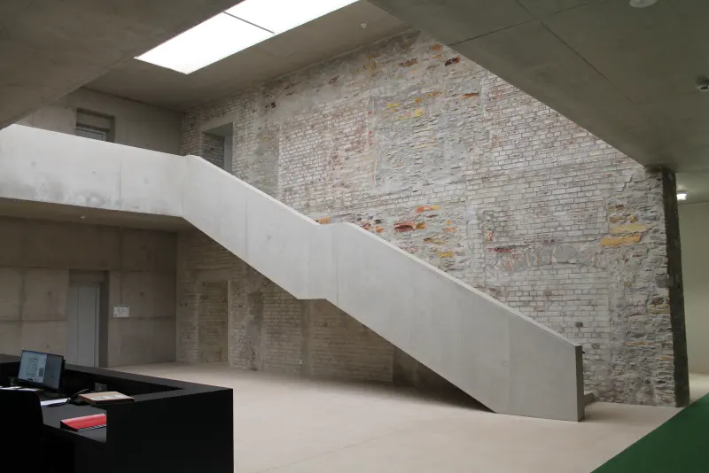 Neue Sichtbetontreppe vor historischem Mauerwerk im sanierten Bestand